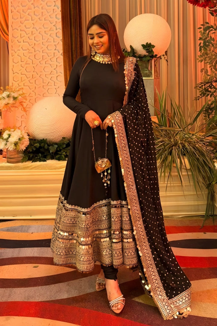Woman in a black and gold traditional outfit with decorative jewelry, standing on a stage.