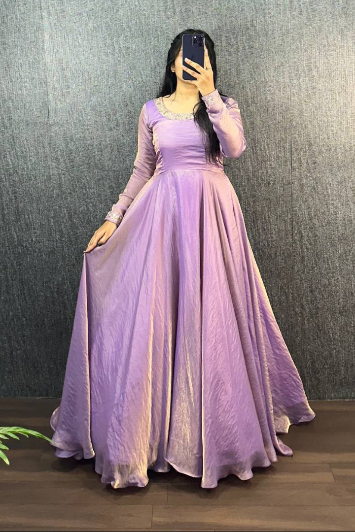 Person wearing a long purple dress against a dark textured wall.