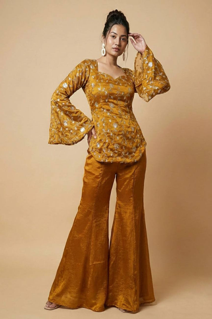 Woman wearing a mustard yellow patterned top and matching flared pants on a beige background