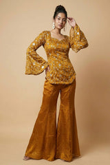 Woman wearing a mustard yellow patterned top and matching flared pants on a beige background