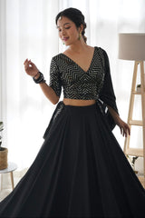 Woman wearing a black and white patterned top with a long black skirt in a bright room.