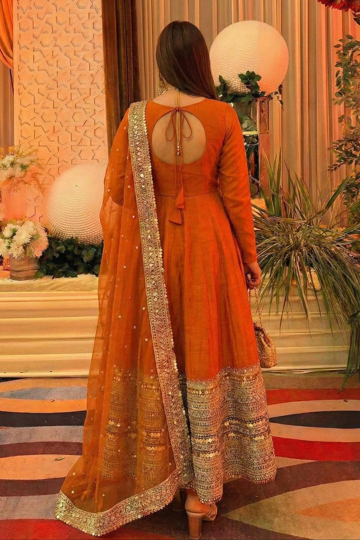 Woman in an orange traditional outfit with a decorative dupatta in a decorated indoor setting.