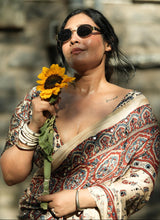Woman in a patterned saree holding a sunflower against a stone wall background