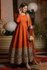 Woman in an orange traditional outfit with gold details in a decorated indoor setting.