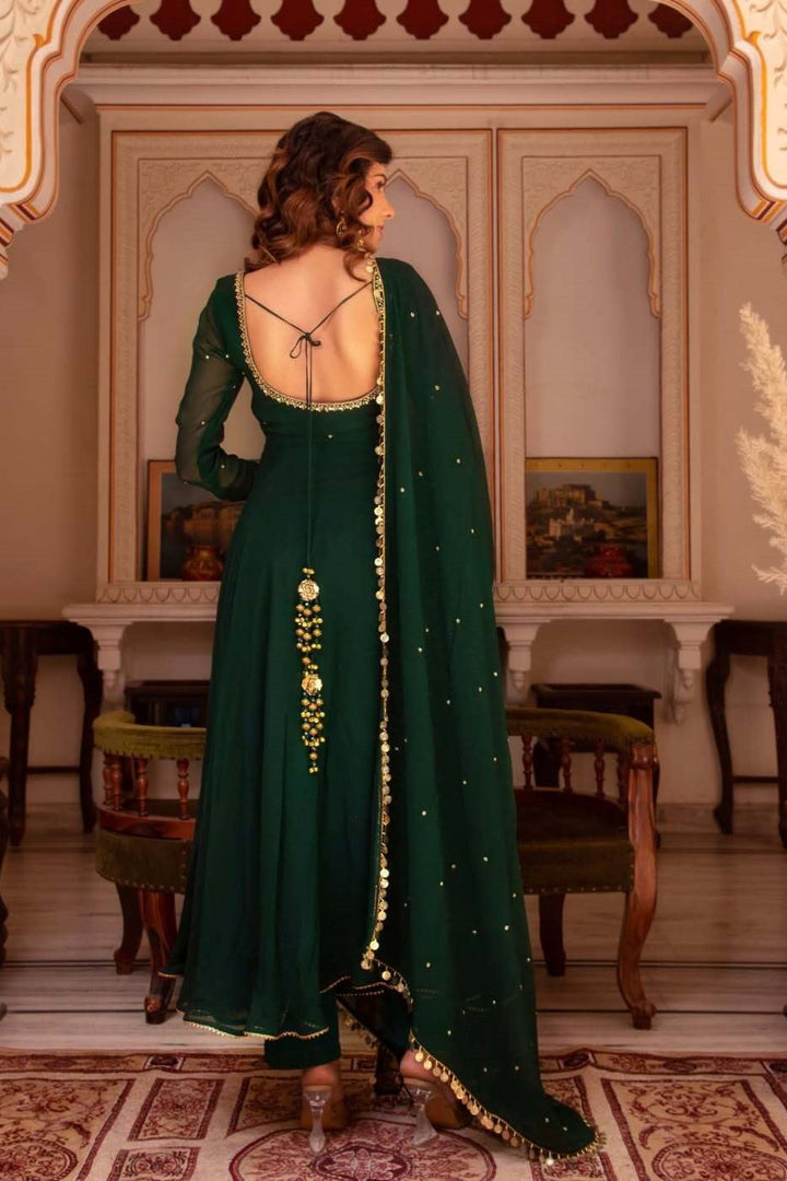 Woman in a green traditional outfit with gold details in an ornate room.