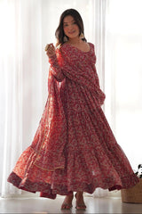 Woman wearing a red patterned dress standing in a bright room with white curtains.