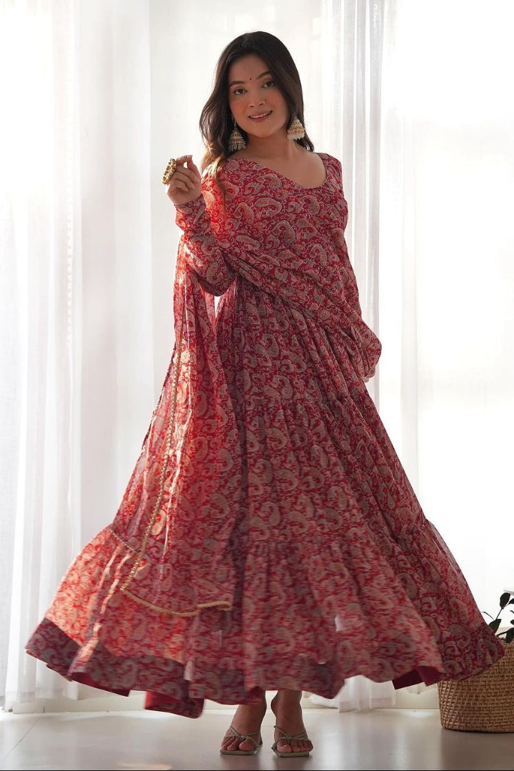 Woman wearing a red patterned dress standing in a bright room with white curtains.