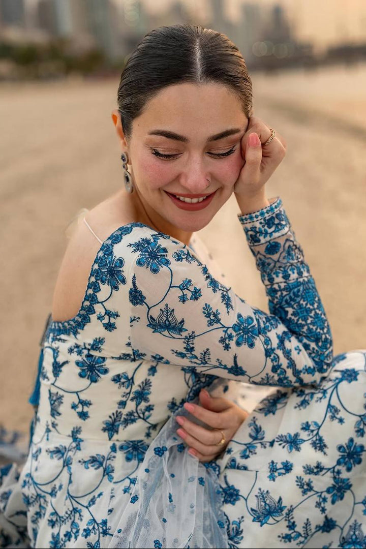 Woman in a blue floral dress sitting on a beach with a blurred cityscape in the background