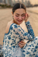 Woman in a blue floral dress sitting on a beach with a blurred cityscape in the background