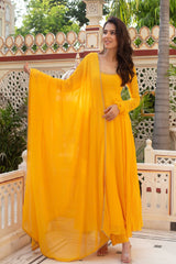 Woman in a yellow traditional outfit standing on a balcony with decorative railing and greenery.