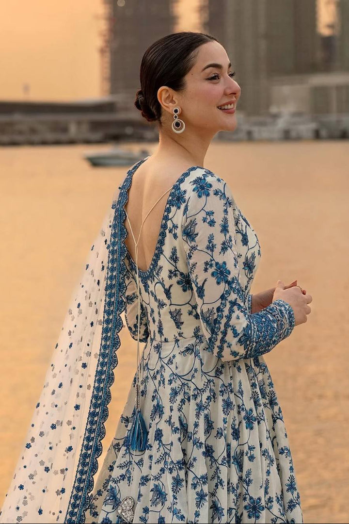 Woman in a blue and white floral dress standing on a beach.