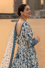 Woman in a blue and white floral dress standing on a beach.