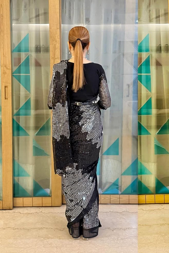 Person wearing a black and white patterned outfit standing in front of a glass door with geometric designs.