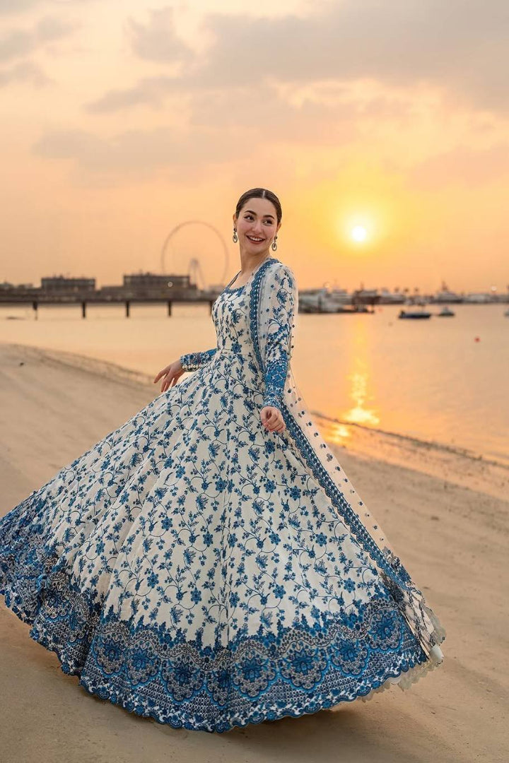 Woman in a blue and white floral dress standing on a beach at sunset.