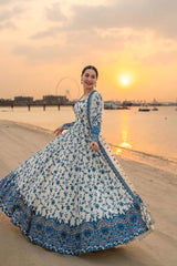 Woman in a blue and white floral dress standing on a beach at sunset.