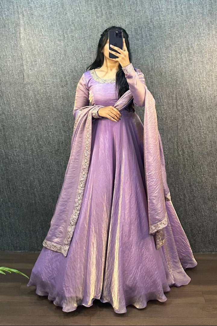 Person wearing a purple traditional outfit with a matching shawl against a gray wall.