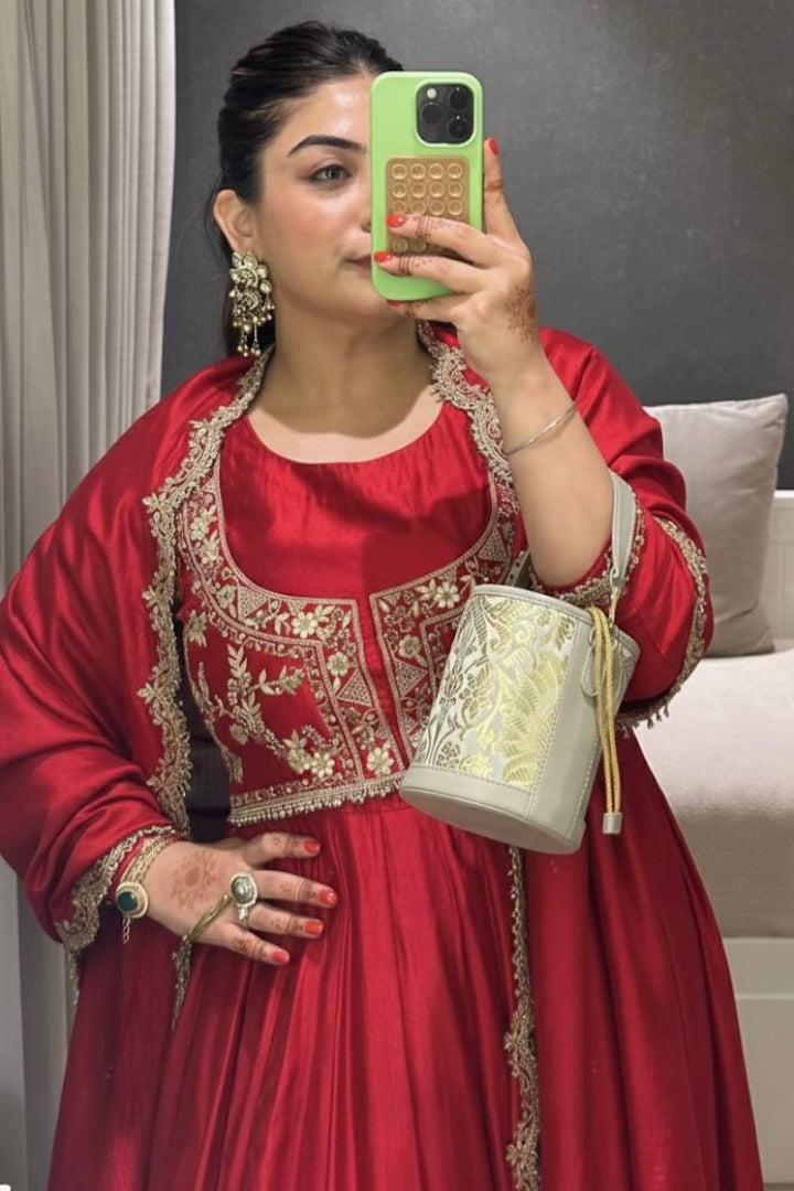 Woman in a red traditional outfit holding a phone and a white bag in a room.