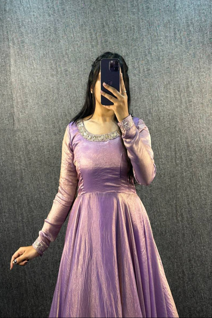 Person wearing a purple dress taking a mirror selfie against a textured gray wall.