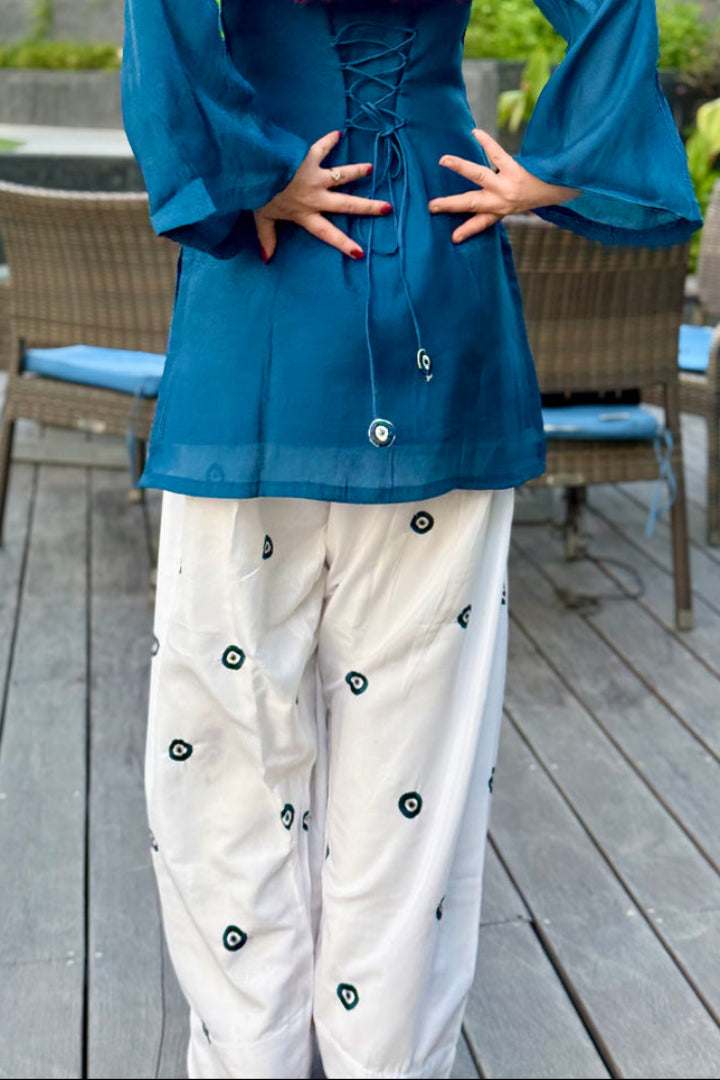 Person wearing a blue top and white pants with black patterns on a wooden deck.