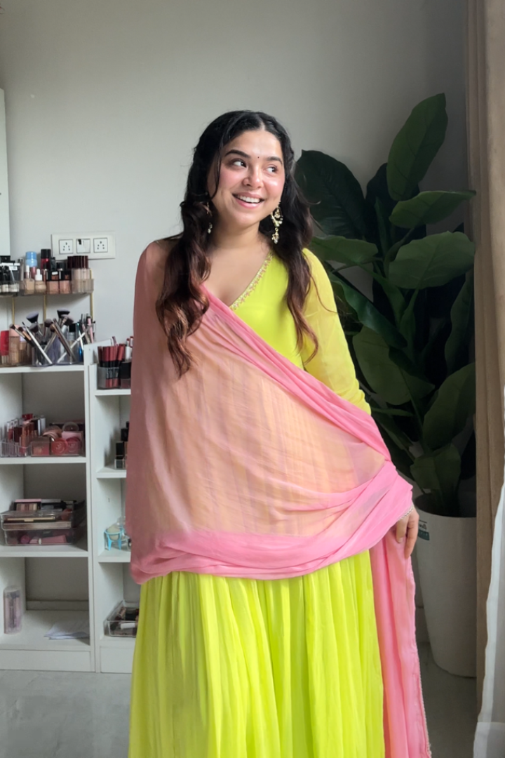 Woman wearing a bright yellow saree with pink blouse in an indoor setting.