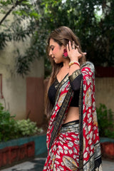 Woman wearing a red and black saree with a floral pattern, standing outdoors.