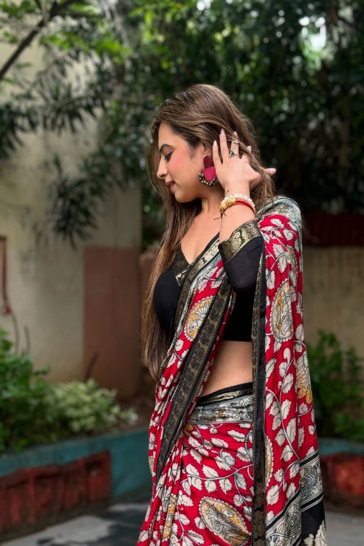 Woman wearing a red and black saree with a floral pattern, standing outdoors.