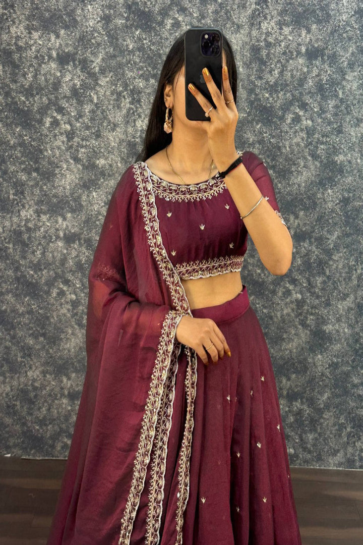 Person wearing a maroon traditional outfit with intricate designs against a textured gray background