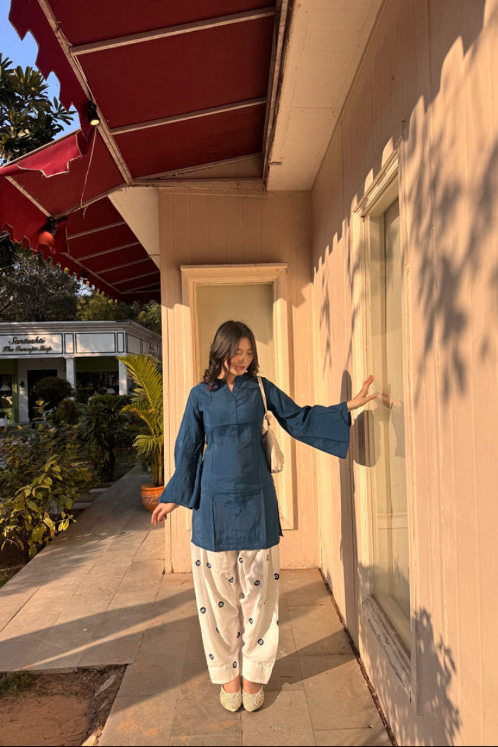 Woman in a blue top and white pants standing outside a building with a red awning.