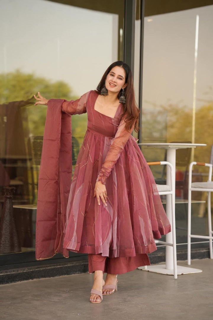 Woman in a maroon dress standing in an outdoor setting with a glass wall.
