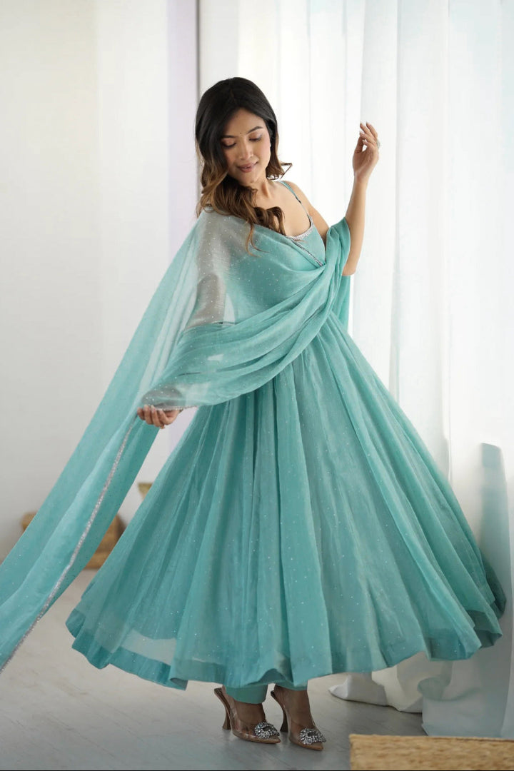 Woman wearing a flowing turquoise dress in a bright room.