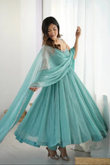 Woman wearing a flowing turquoise dress in a bright room.