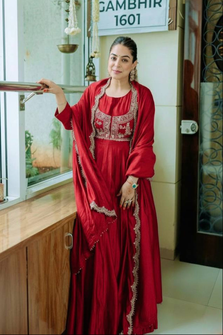 Woman in a red traditional outfit standing indoors with a sign in the background.