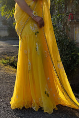 Yellow saree with floral patterns on a person, standing outdoors.