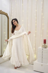 Woman in a white traditional outfit standing in a softly lit room with decorative lights.