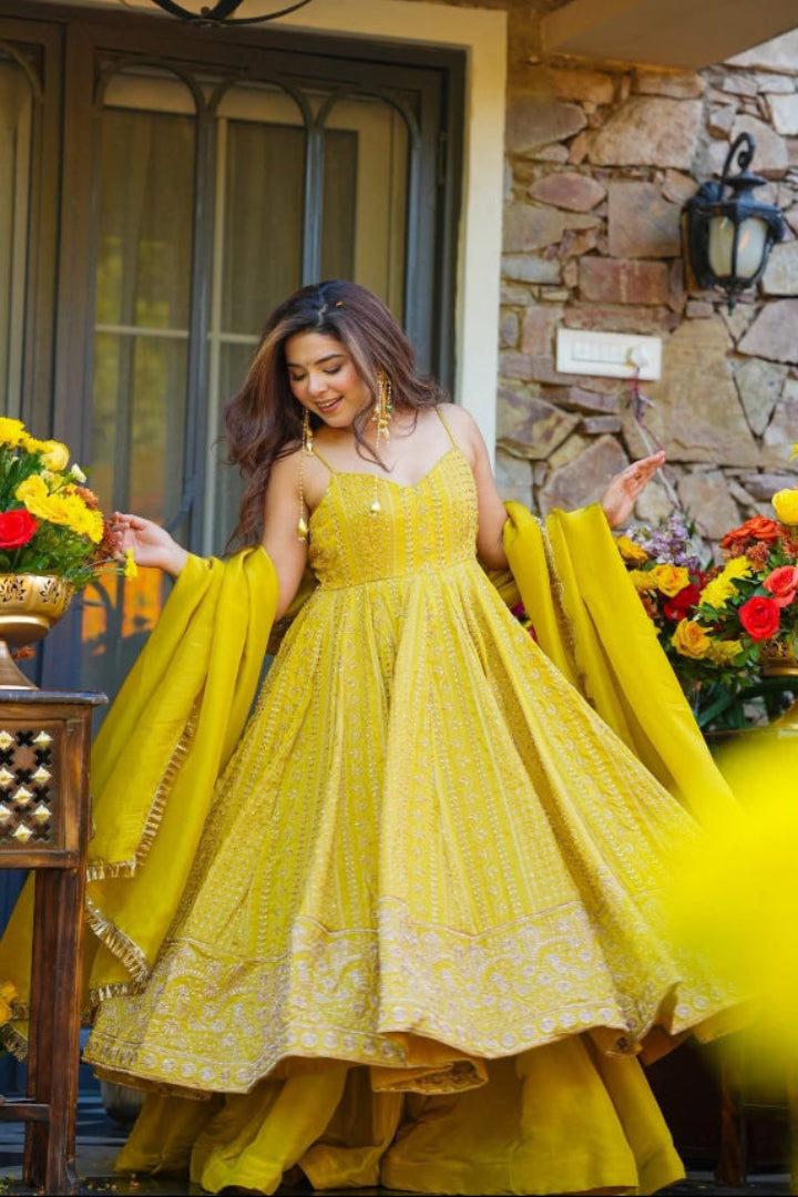 Woman in a yellow dress standing in front of a stone wall with floral arrangements.
