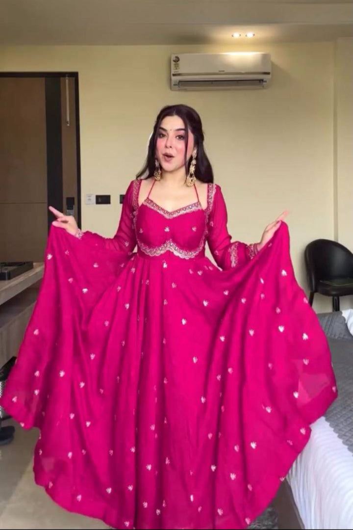 Woman in a bright pink traditional outfit with white patterns in a room.