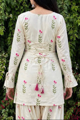 Woman wearing a white dress with floral patterns against a green leafy background