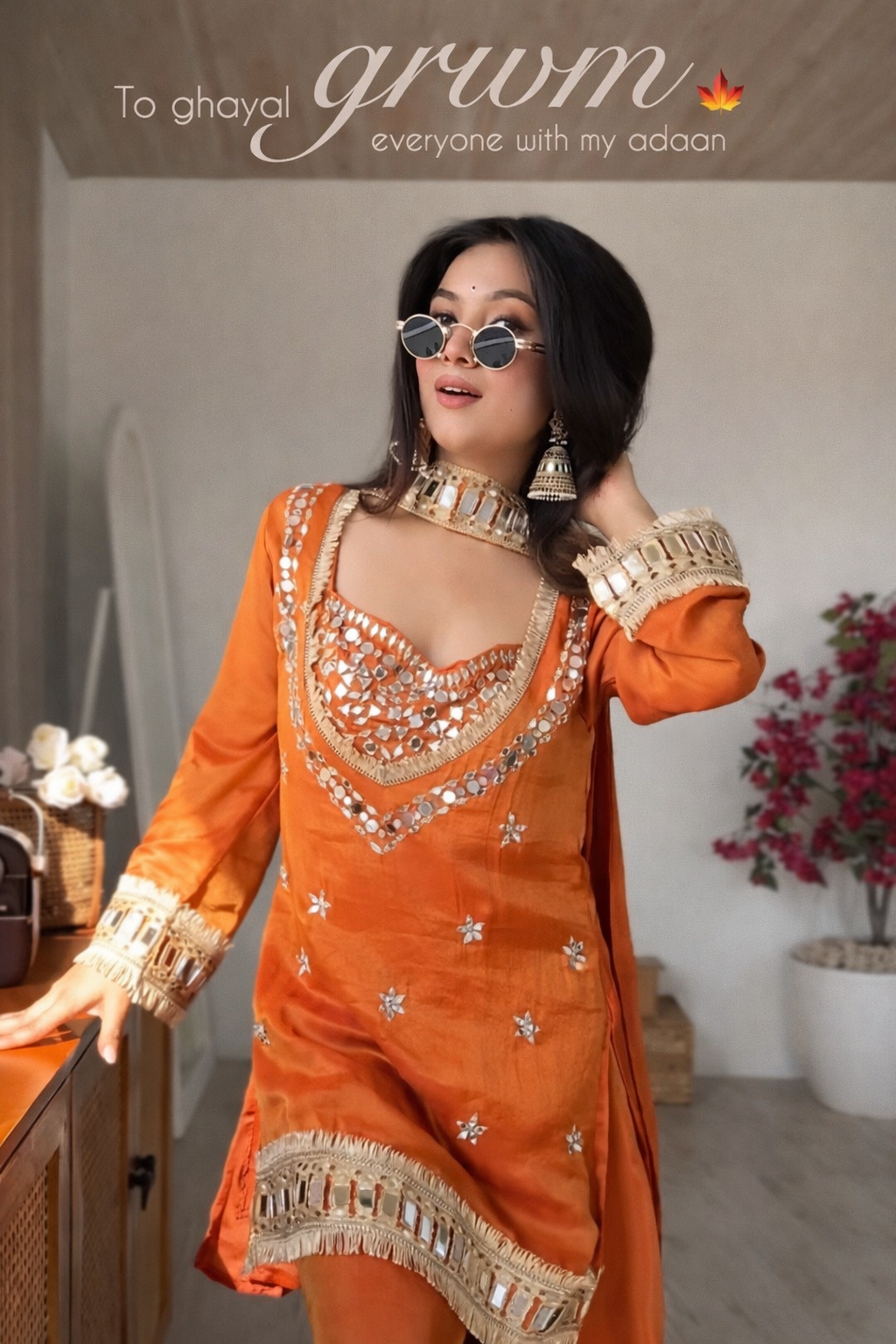 Woman in an orange traditional outfit with gold embroidery in a room setting.