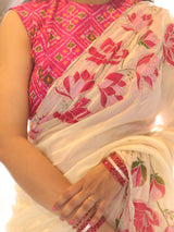 A close-up of a woman wearing a traditional Indian saree with a pink floral embroidered blouse and a white saree featuring pink lotus motifs.