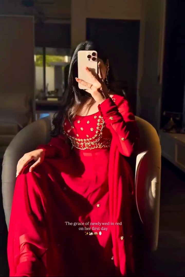 Person wearing a red outfit with gold details, sitting in a room.