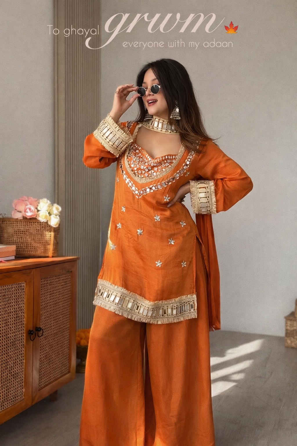 Woman in an orange traditional outfit with gold details, standing indoors.