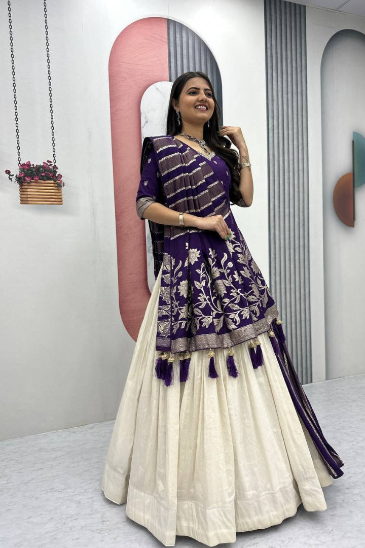 Woman wearing a purple and white traditional outfit in a minimalistic room.