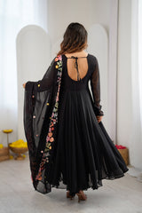 A woman viewed from behind wearing a black long-sleeve maxi dress with an open back and holding up a matching sheer black dupatta decorated with colorful floral embroidery.