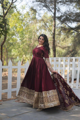 Woman in a maroon traditional outfit with gold details standing outdoors near a white picket fence.