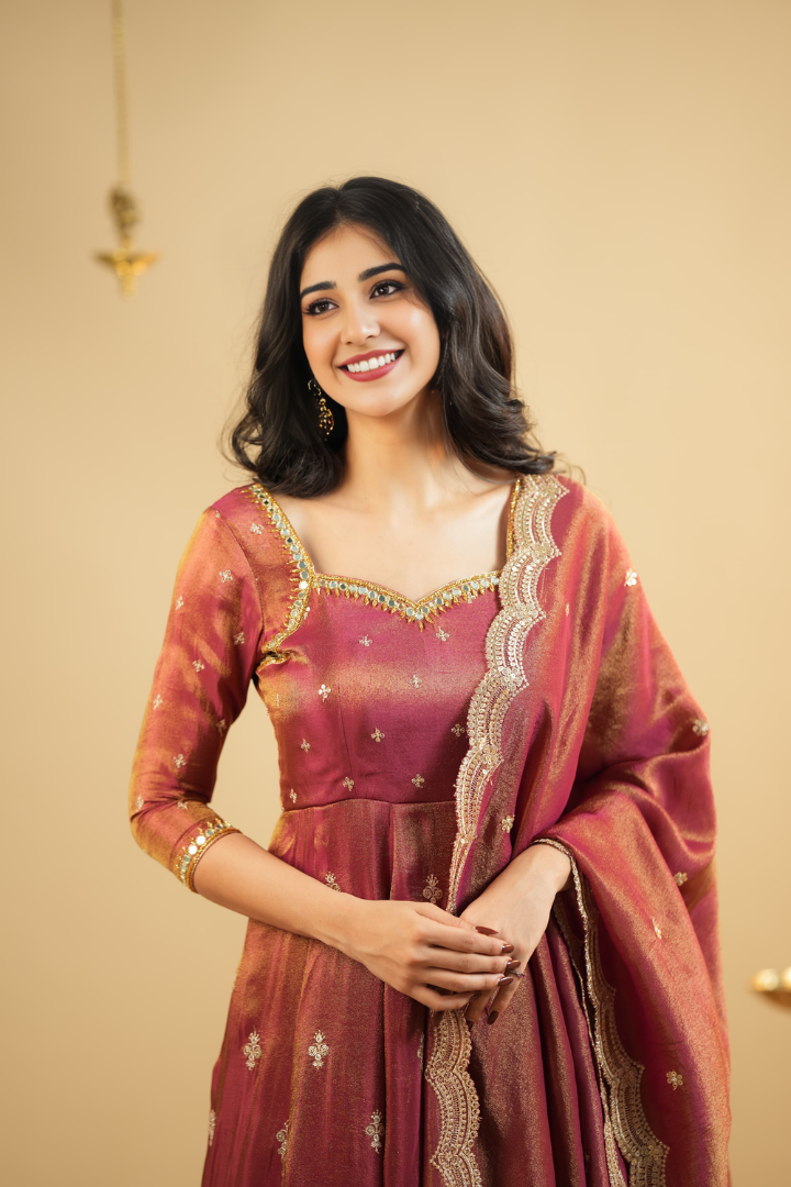 Woman in traditional maroon and gold outfit with a beige background