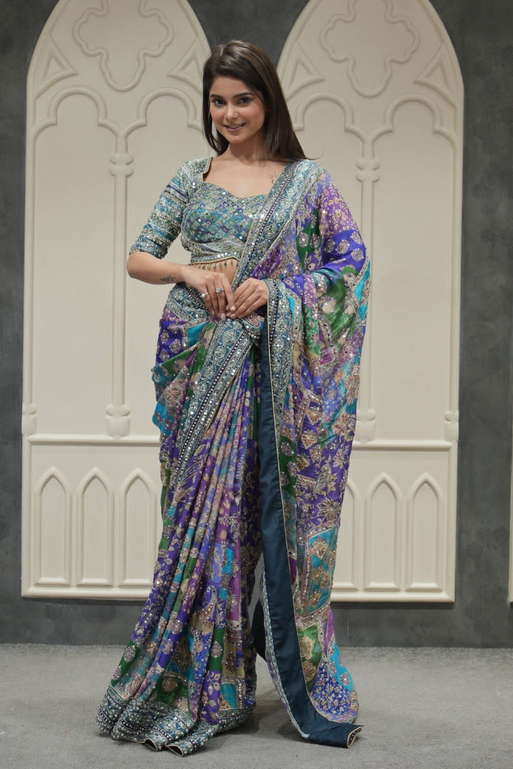 Woman wearing a colorful saree in front of decorative walls.
