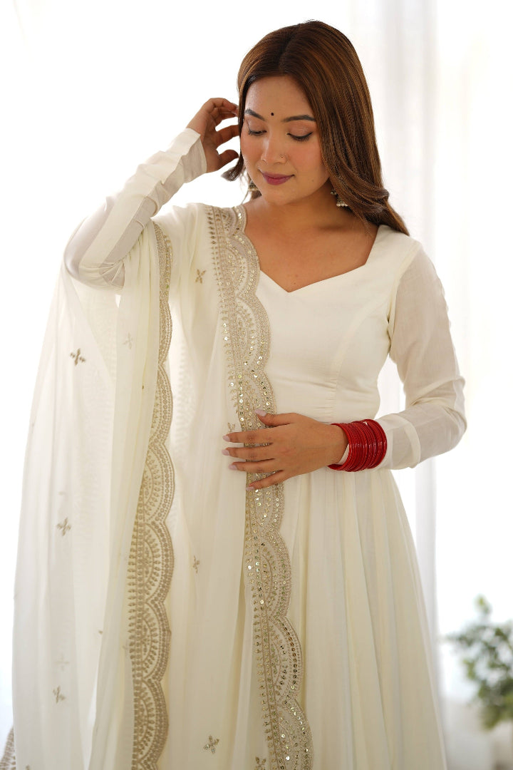 Woman wearing a white traditional outfit with a matching dupatta, indoors.