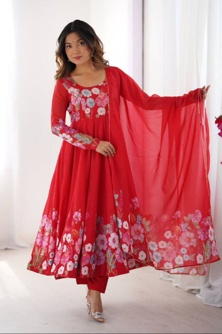 Woman wearing a red floral dress holding a matching dupatta against a white curtain background