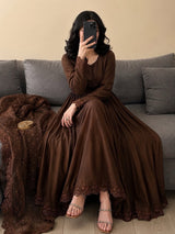 Woman in a brown dress sitting on a gray couch with a beige wall background