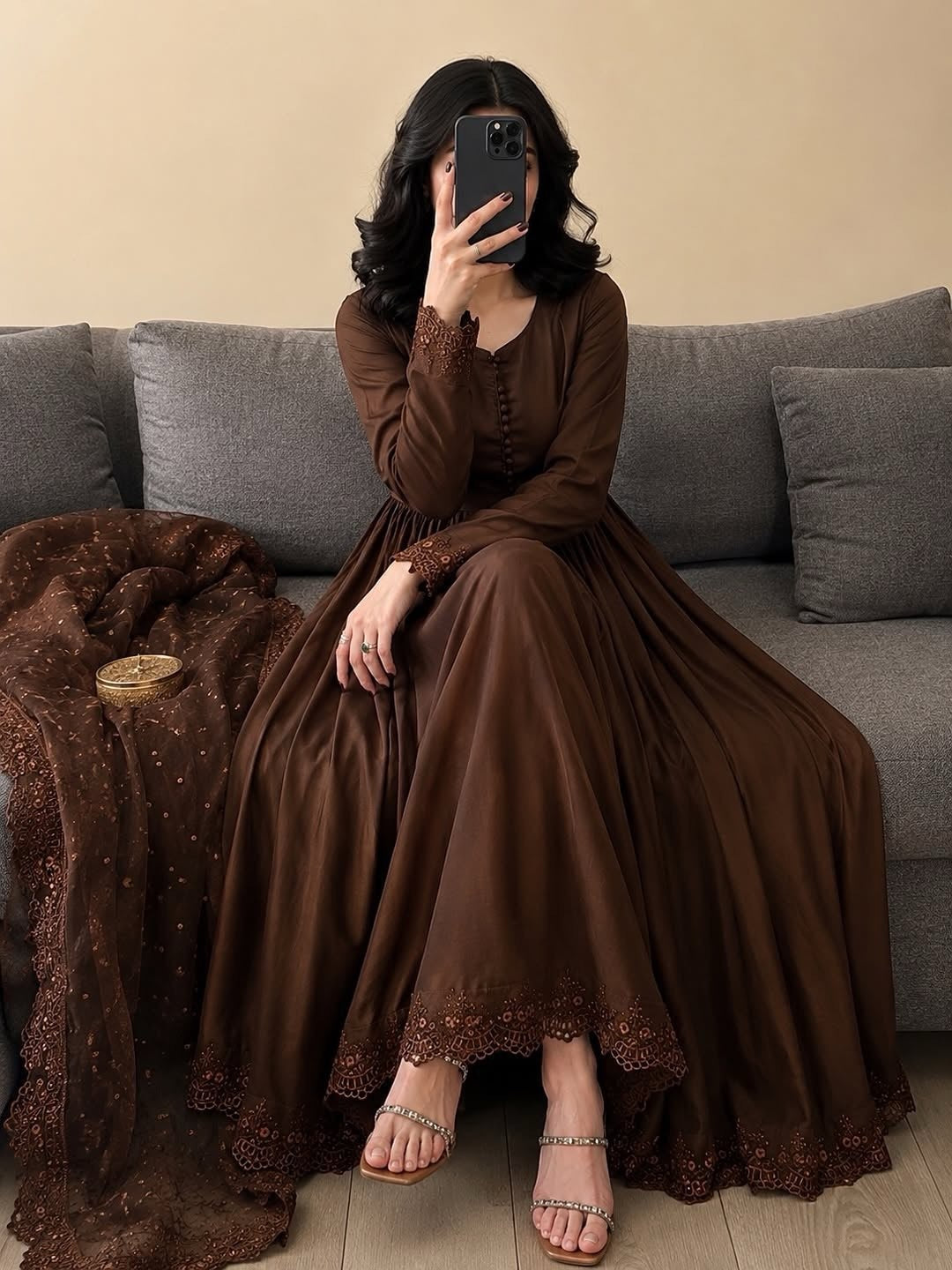 Woman in a brown dress sitting on a gray couch with a beige wall background